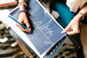 Woman analyzing financial graph with a printout on a glass table holding a pencil.